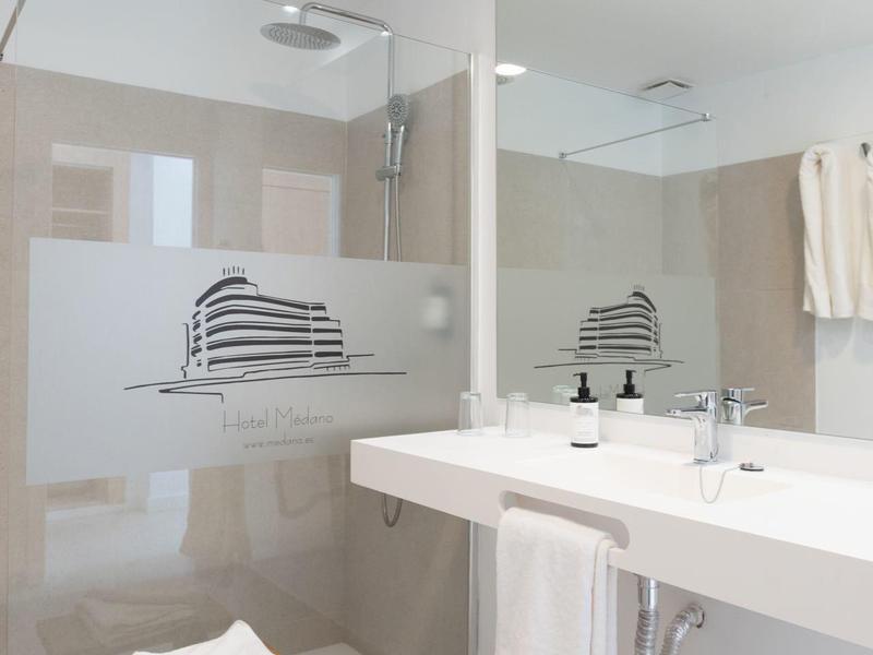 Bagno luminoso con ampia doccia, lavabo, specchio e sgabello di legno con asciugamani.