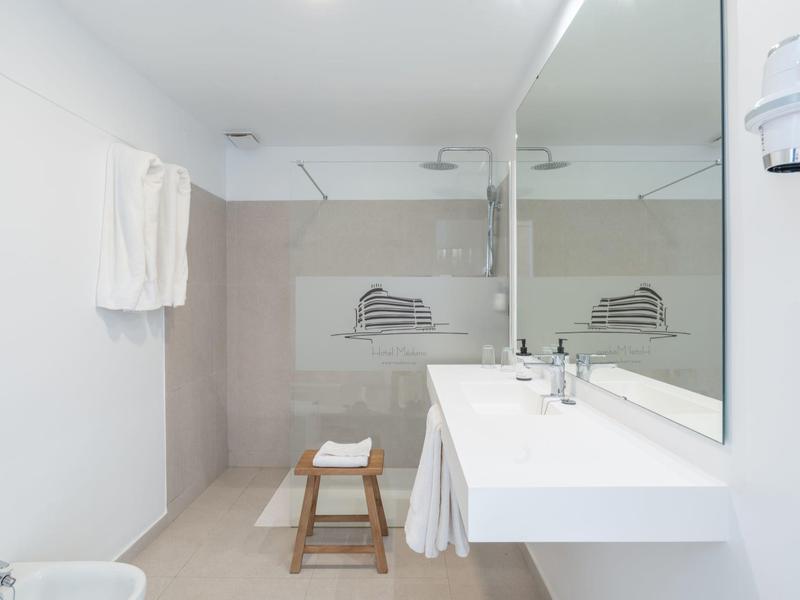 Bagno bianco moderno con grande specchio e doccia aperta con sgabello di legno.
