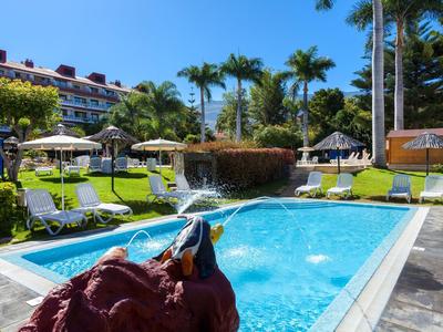 Piscina esterna con lettini e palme accanto a un edificio dell'hotel sotto un cielo azzurro.