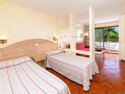 Hotelový pokoj se dvěma jednolůžky, dřevěným nábytkem a přístupem na balkon s terasou.