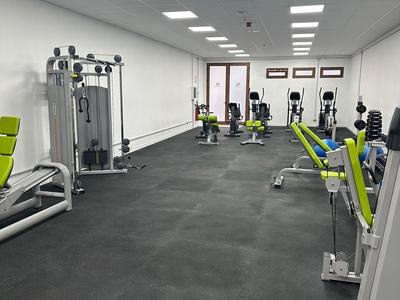 Gimnasio moderno con equipo de entrenamiento y piso negro-gris en una habitación luminosa.