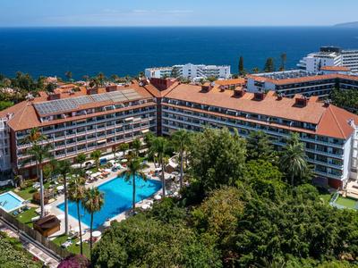 Grand hôtel avec toit rouge, piscine et vue sur la mer bleue.