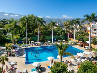 Grand bassin d'hôtel avec chaises longues, parasols et palmiers dans un cadre tropical.