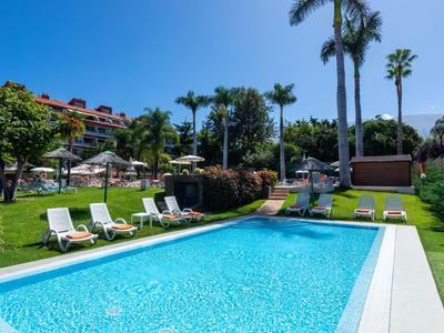 Piscine bleue claire avec chaises longues et palmiers dans une zone hôtelière.