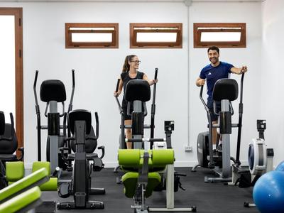 Intérieur d’une salle de sport avec deux personnes sur des elliptique et équipement moderne.