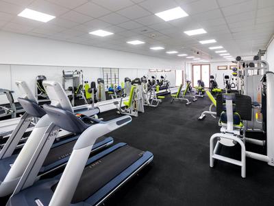 Salle de sport moderne avec divers appareils d'entraînement et éclairage lumineux.