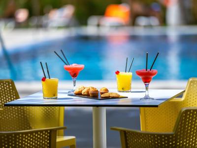 Boissons et croissants sur une table près d'une piscine d'hôtel avec des chaises jaunes.