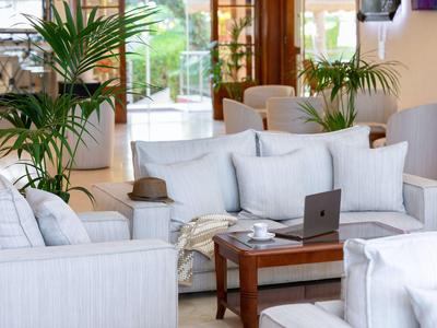 Chambre d'hôtel moderne lumineuse avec canapés blancs, table en bois et plantes.