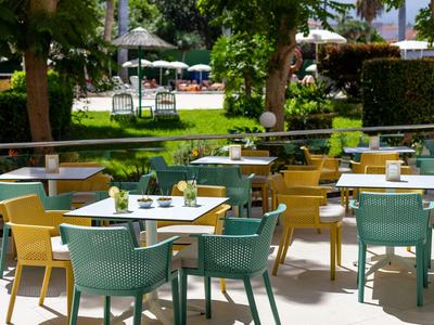 Restaurant en plein air avec des chaises et des tables colorées dans un jardin verdoyant.