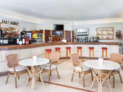 Espace bar d'hôtel lumineux avec des tabourets hauts, des tables rondes et des chaises tressées.