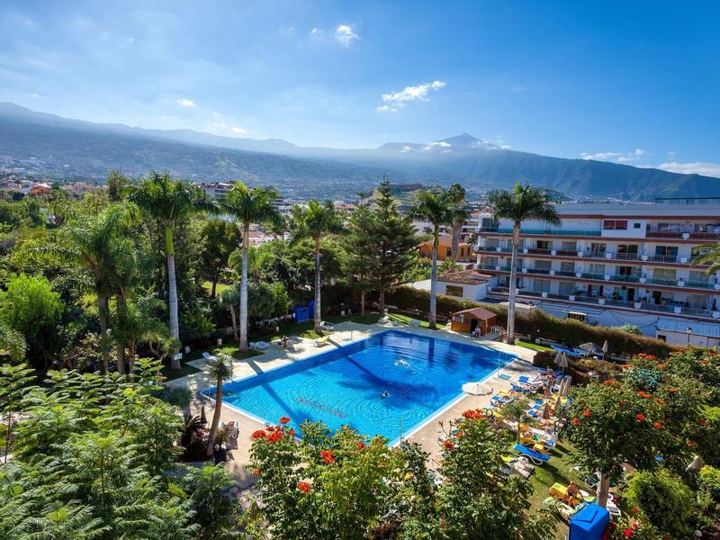 Pohled na bazén v tropickém hotelu s horami v pozadí.