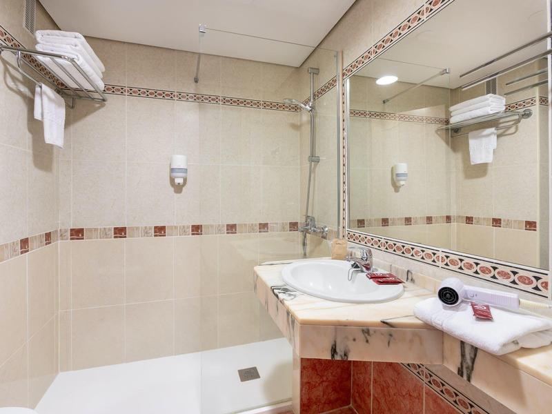 Moderní koupelna se sprchou, velkým zrcadlem a umyvadlem v teplých tónech.