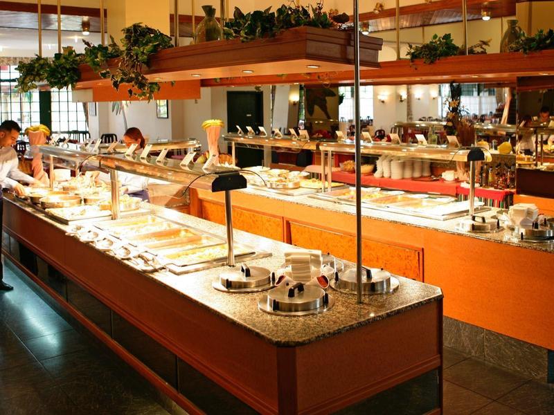 Bufet w dużej jadalni z różnymi potrawami i osobą nakładającą jedzenie.