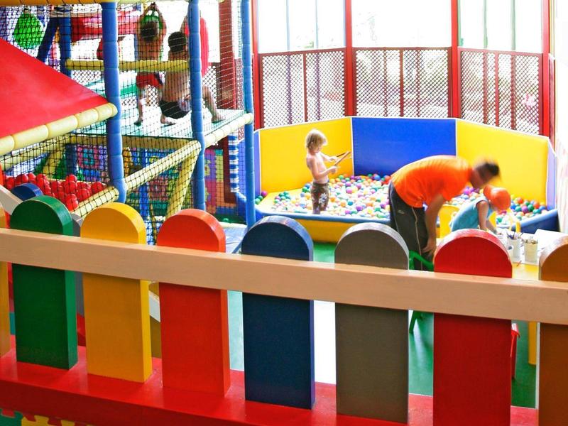 Kolorowy, kryty plac zabaw dla dzieci z siatką wspinaczkową i basenem z piłkami w jasnym pomieszczeniu.