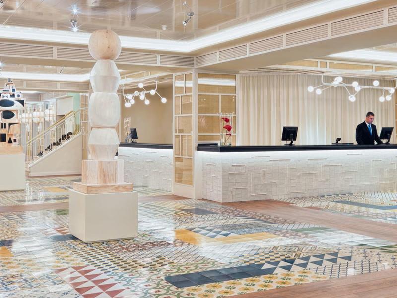 Przestronne lobby hotelowe z wzorzystą podłogą, białymi filarami i recepcją z personelem.