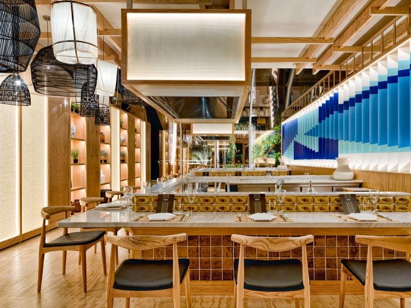 Nowoczesna jadalnia hotelowa z drewnianymi stołami, krzesłami i dekoracyjnym oświetleniem.
