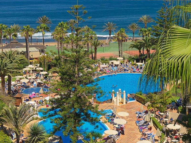 Ośrodek z basenami otoczonymi palmami i leżakami blisko oceanu.