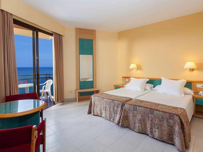 Camera d'albergo spaziosa con letto doppio, tavolo rotondo, vista mare e balcone.