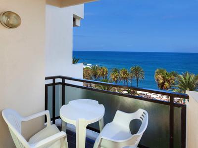 Balcone con tavolo rotondo e sedie, vista sul mare e palme.