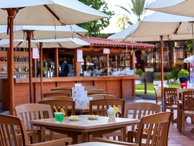 Terrazza esterna di un bar con ombrelloni bianchi e mobili in legno chiaro.