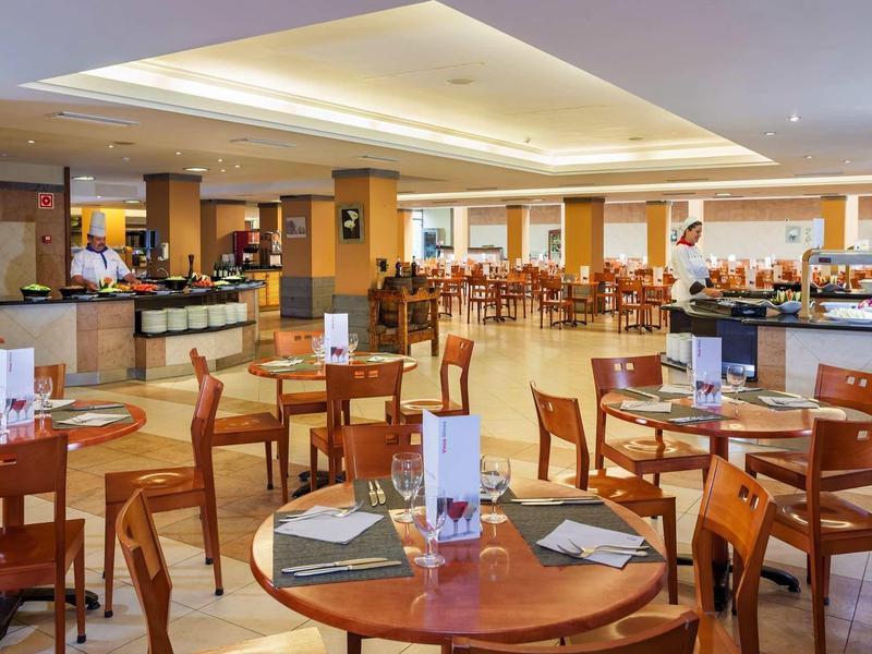 Ampia sala ristorante con tavoli e sedie in legno, illuminazione calda.