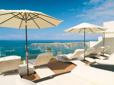 Sun loungers and umbrellas on a terrace overlooking the sea under a blue sky.