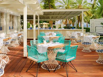Espace extérieur ouvert d'un restaurant avec chaises blanches et turquoise sur terrasse en bois en milieu tropical