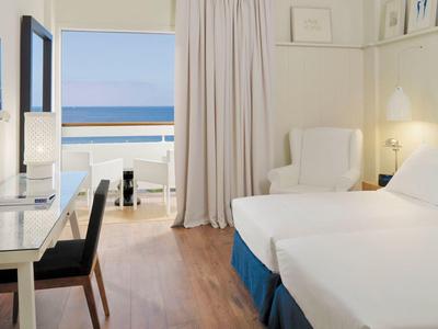Cozy hotel room with twin beds, desk, and ocean view through balcony door.