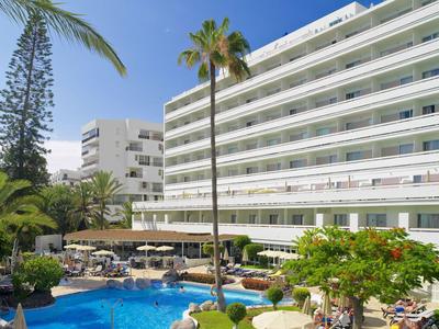 Complexe hôtelier moderne avec grande piscine, palmiers et chaises longues sous ciel bleu