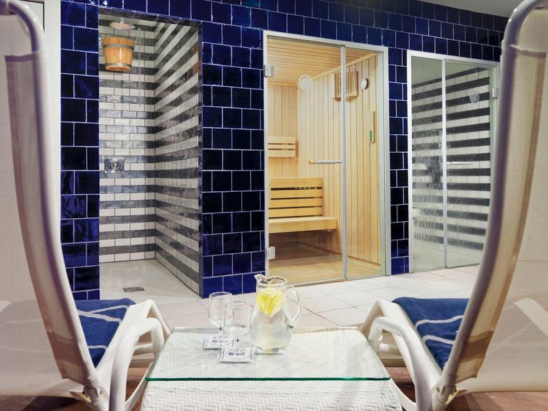 Indoor relaxation area with lounge chairs and a view into a wooden sauna room.