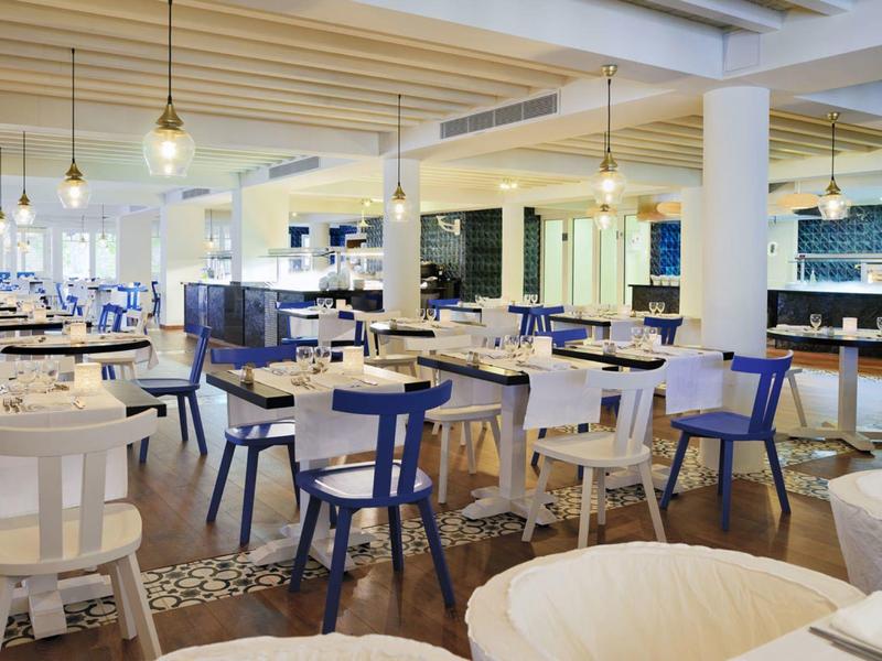 Modern hotel restaurant with white and blue chairs and wooden tables under hanging lights.