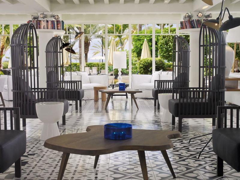 Modern outdoor seating area with black chairs, white cushions, and a wooden table under a covered patio.
