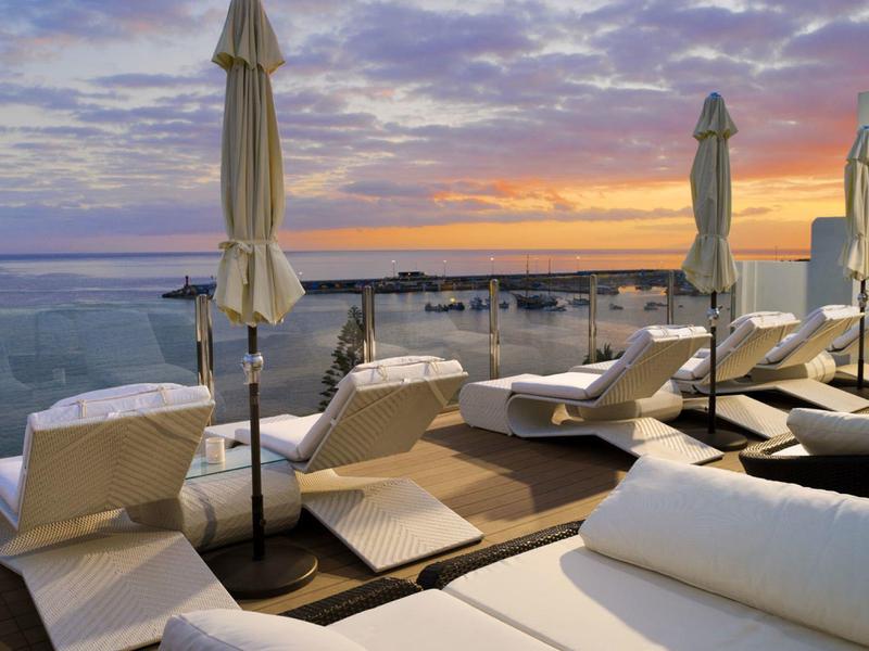 Sunset view from a terrace with lounge chairs and closed umbrellas by the sea.