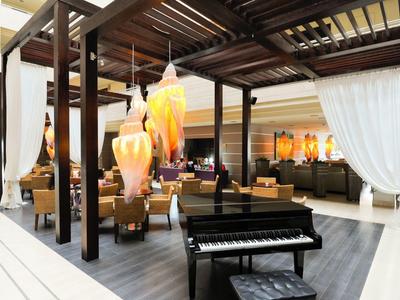 Nowoczesna przestrzeń lounge z czarnym pianinem, wiszącymi lampami i białymi zasłonami.