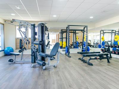 Salle de sport moderne avec machines de musculation, haltères et bancs sur un sol en bois clair.
