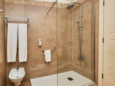 Modern hotel bathroom with walk-in shower, white towels, and beige tiled walls.