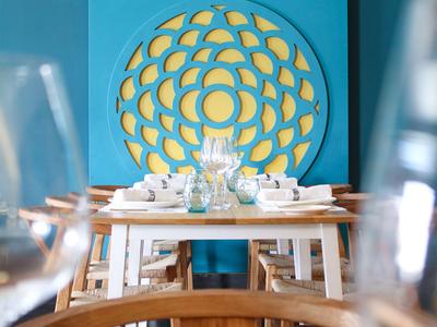 Modern dining area with white tables and a blue wall decoration featuring a yellow geometric pattern.