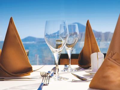 Elegancko nakryty stół z brązowymi serwetkami, kieliszkami i widokiem na morze.