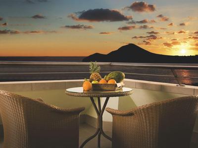 Zachód słońca nad morzem z tarasem, stołem i miską owoców na pierwszym planie.
