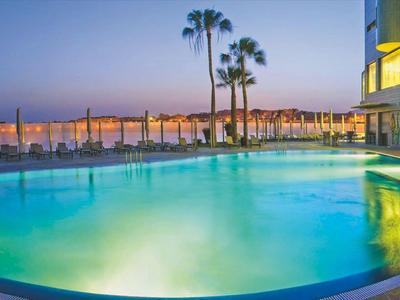 Oświetlony basen hotelowy o zmierzchu z palmami i morzem w tle