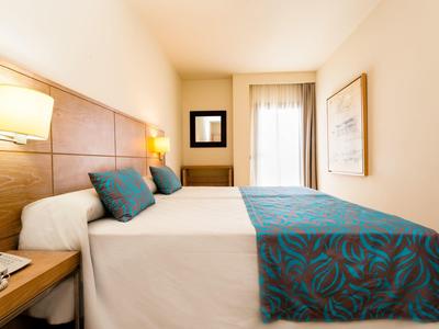 Jasny pokój hotelowy z dużym łóżkiem, drewnianym zagłówkiem i niebieskimi poduszkami w wzory.