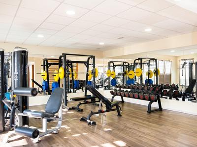 Nowoczesna siłownia z ciężarami, ławkami do hantli i sprzętem na drewnianej podłodze.