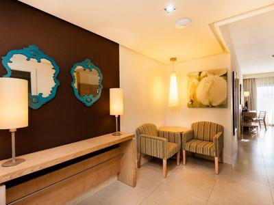 Przytulna lobby hotelowa z fotelami, stołem, lustrami i ciepłym oświetleniem.