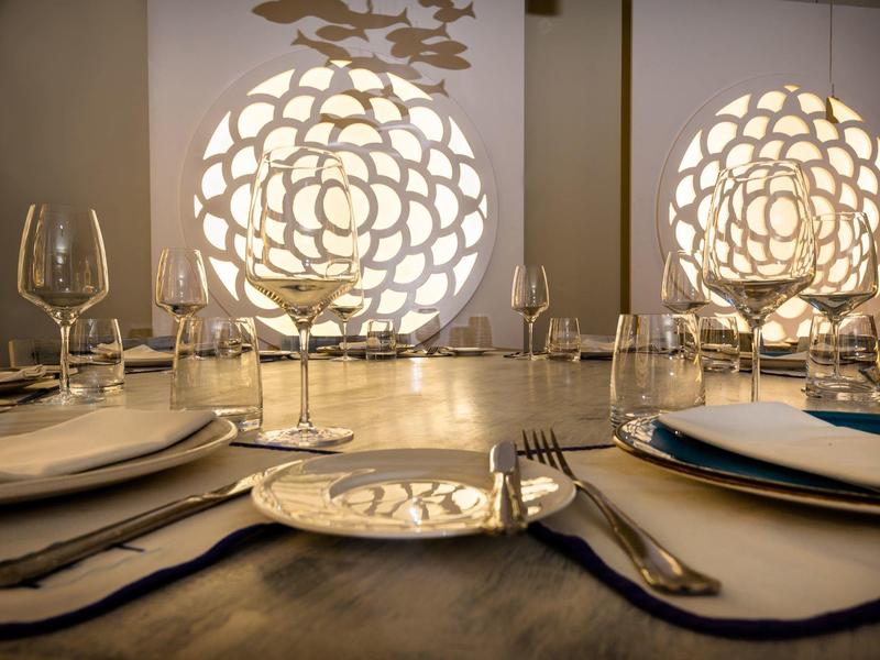 Elegancko nakryty stół z kieliszkami do wina i wody przed dekoracyjnym oświetleniem ściennym.