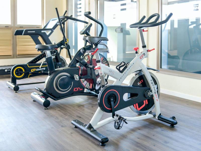 Trzy nowoczesne rowery treningowe w jasnym pokoju z dużymi oknami.