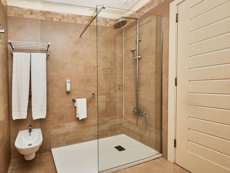 Nowoczesna łazienka z otwartym prysznicem, bidetem i białymi ręcznikami na ścianie