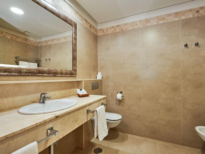 Jasno oświetlona łazienka z umywalką, dużym lustrem i toaletą.