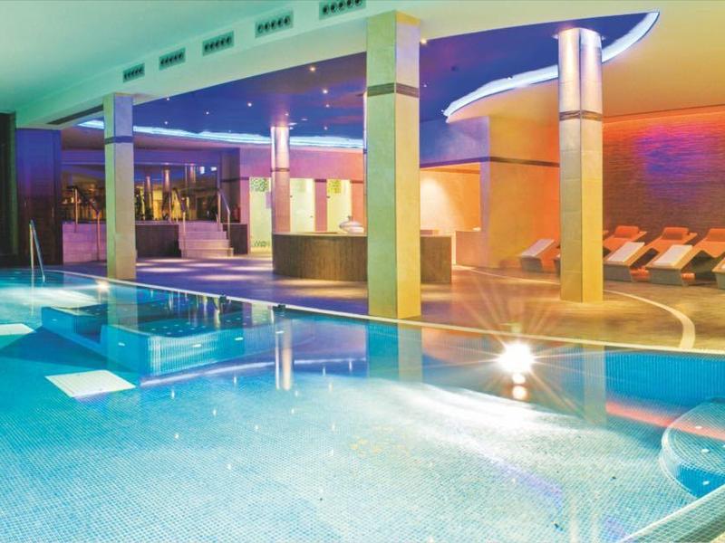 Basen kryty z niebieskimi płytkami, miejscem do siedzenia i dużymi oknami z widokiem na zewnątrz.