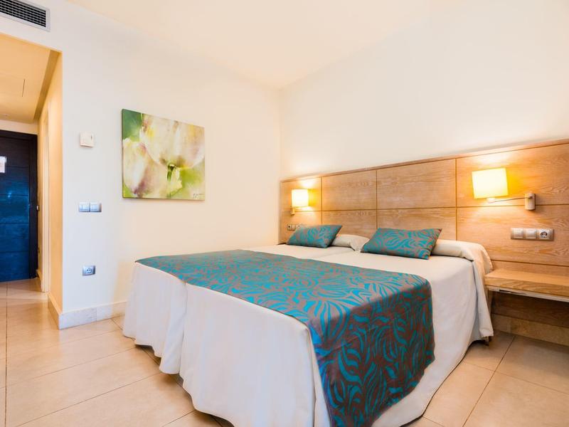 Jasny pokój hotelowy z podwójnym łóżkiem, drewnianą dekoracją i nowoczesnym oświetleniem.