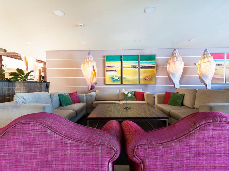 Jasny, nowoczesny salon z różowymi fotelami, sofą i kolorową sztuką ścienną w hotelu.